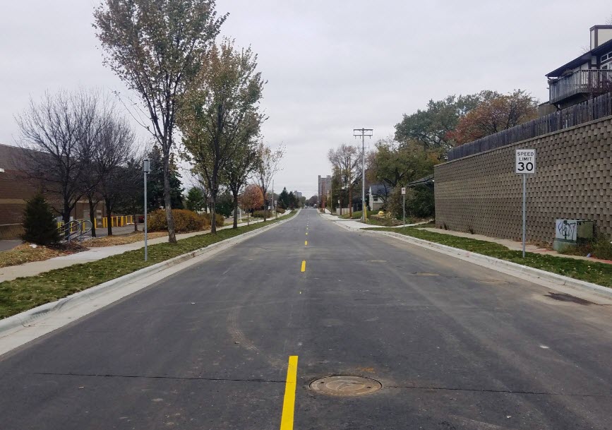 Paved street surrounded by a tree and two industrial buildings.