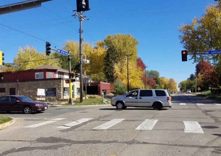 City intersection with cars driving and a white striped pedestrian crossing