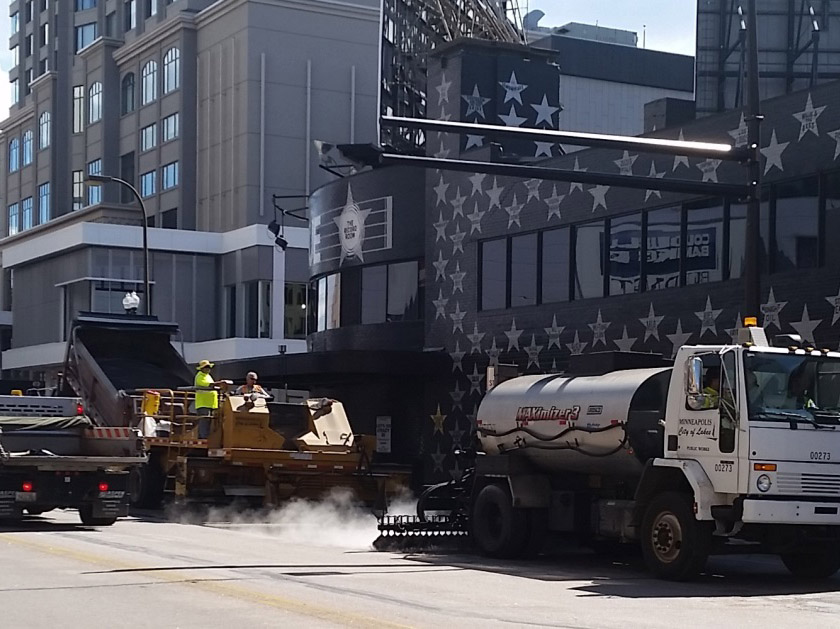 Workers seal coating a road.