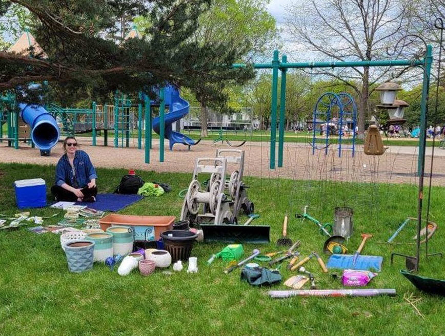 Person sitting under tree near garden tools available as part of a garden swap.