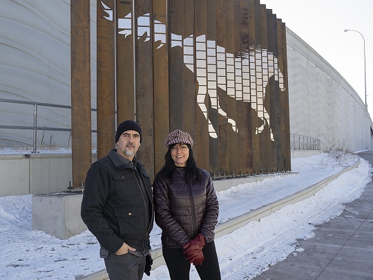 Two people standing outside in front of a sculpture Two people standing outside in front of a sculpture