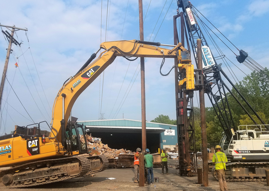 Piles (long support pipes) being driven into the ground with a piece of construction equipment.