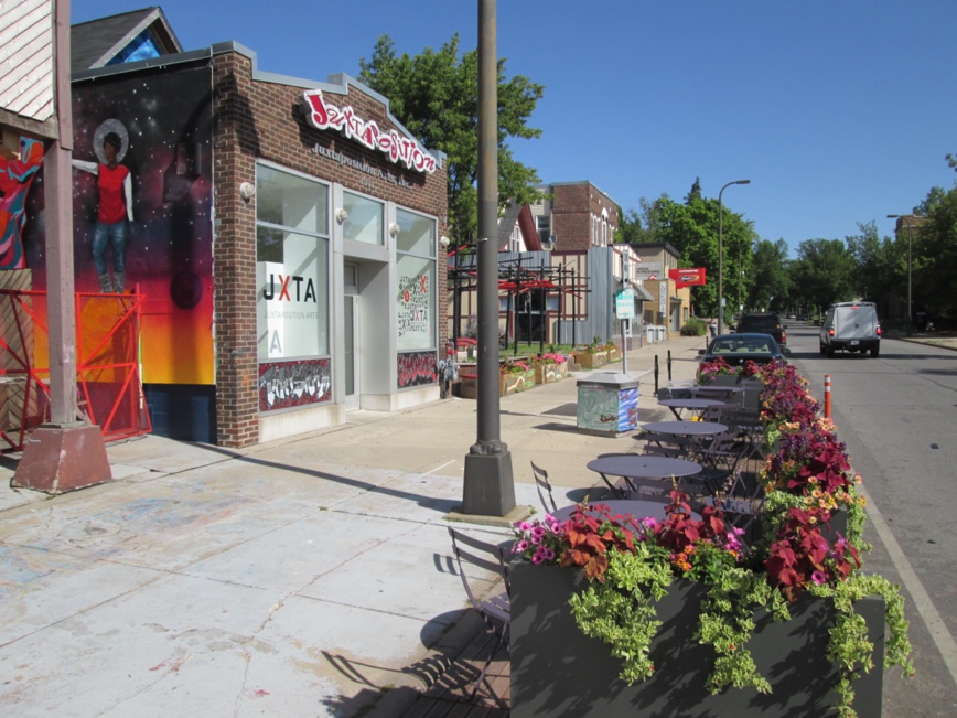 Juxtaposition Arts - streetfront view of building - tables and blooming flower in pots on sidewalk