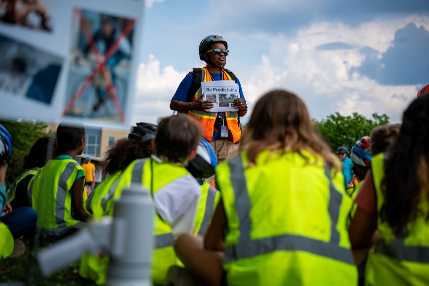 children wearing yellow vests listening to a person