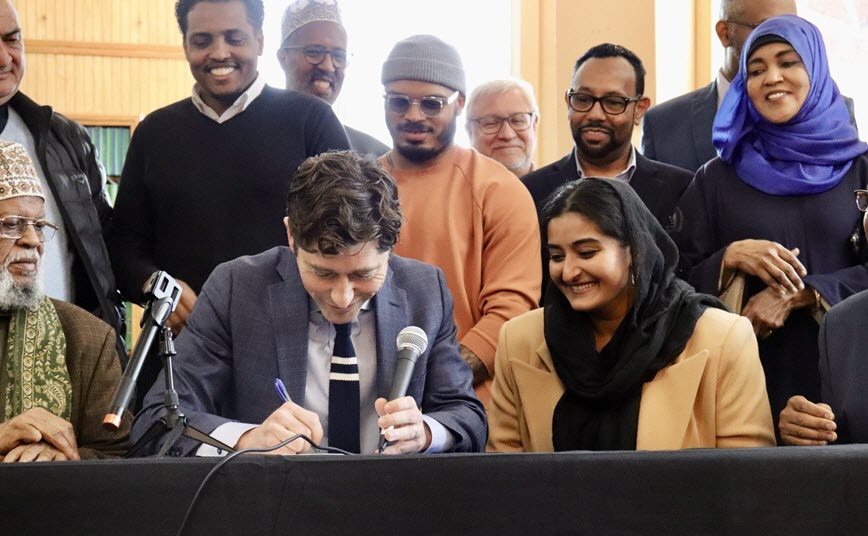 Mayor signing document with people watching.