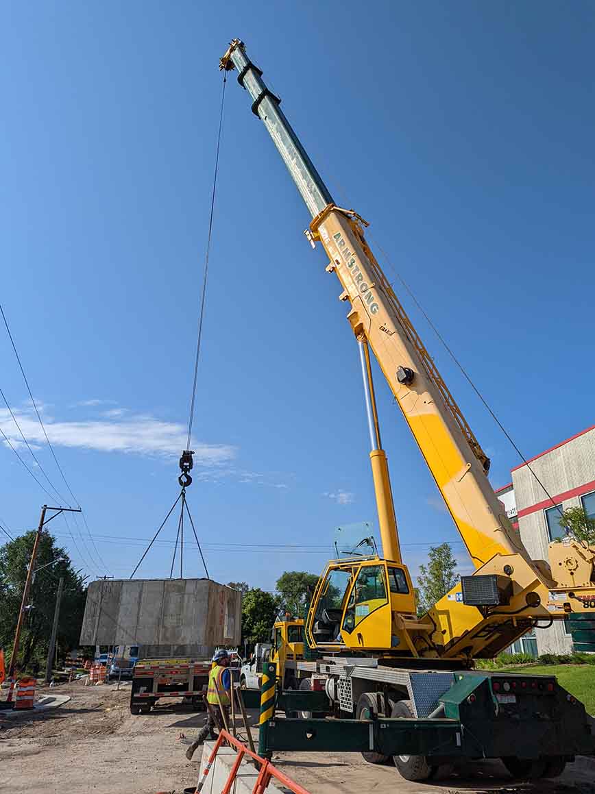 A crane lifts a concrete box structure off of a truck and prepares for installation. A crane lifts a concrete box structure off of a truck and prepares for installation.