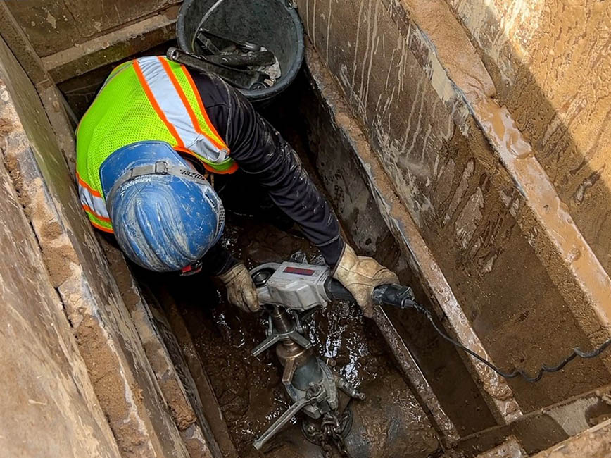 A worker in a trench replacing a water service line