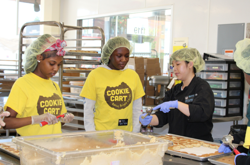 Three people making cookies at cookie cart