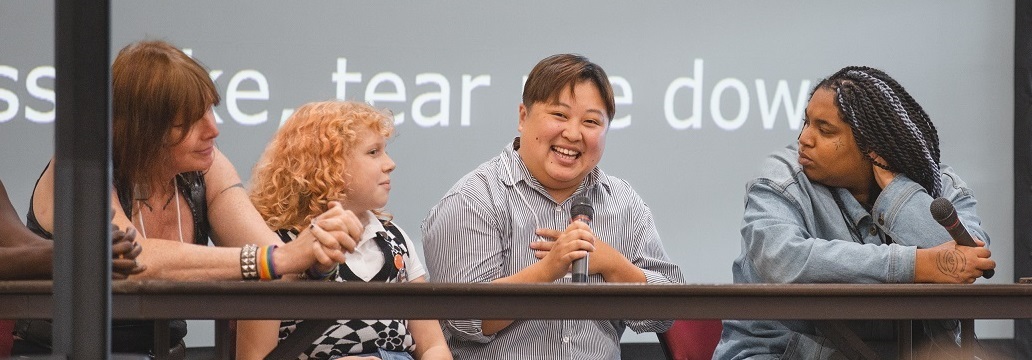 Smiling person seated on speakers' panel holding microphone 