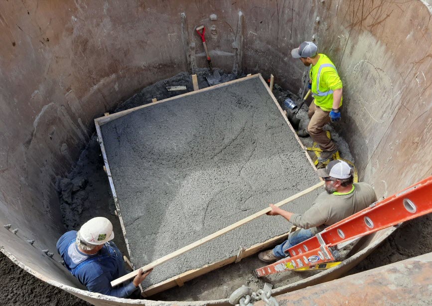 Workers leveling a square of concrete in a manhole