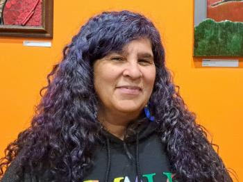 Lori Green with long black wavy hair in front of an orange wall.