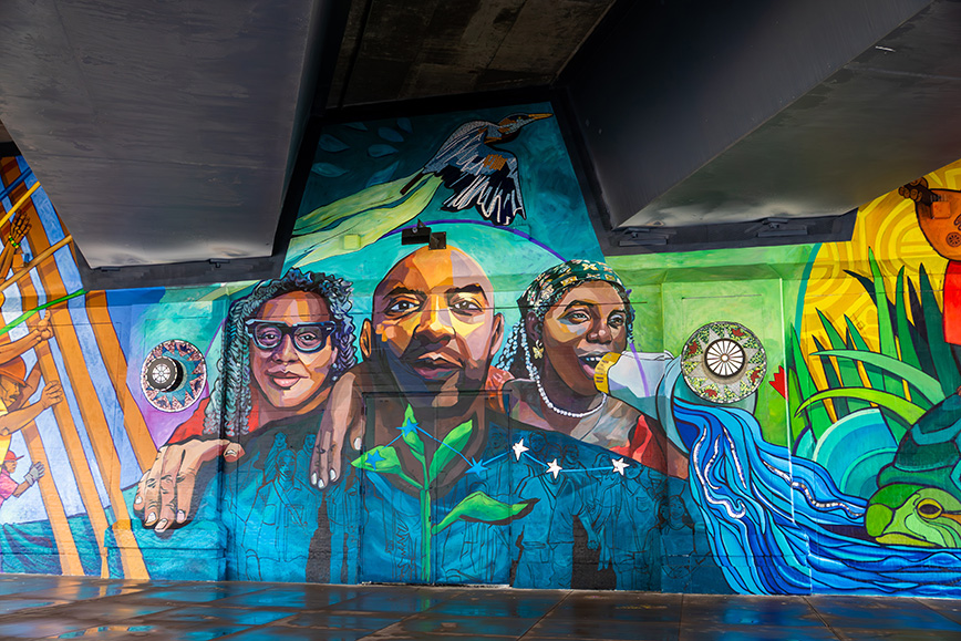 A mural of three people. A woman on the left rests her hand on a man&rsquo;s shoulder. On his right is a woman holding a megaphone to her mouth.