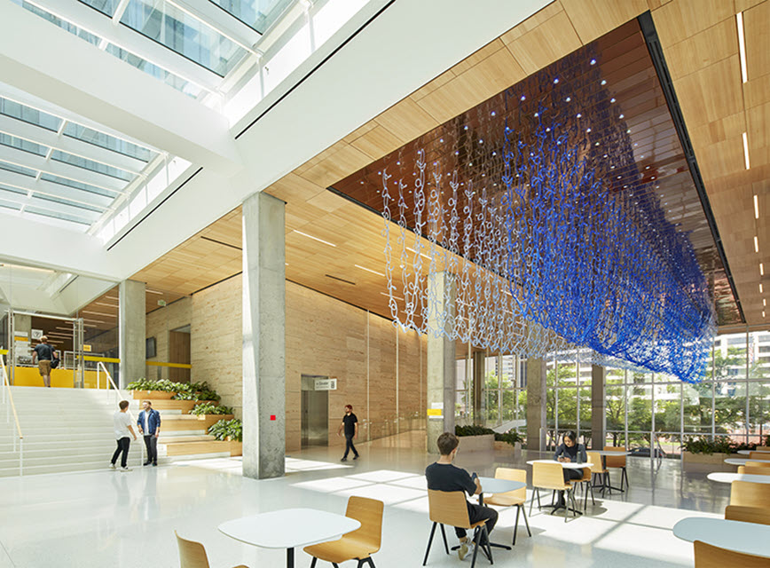 Large ceiling sculpture of clear blue chains in U-shaped loops in a two-story room with open stairs. Photo credit: Current Conditions by Tristan Al-Ha