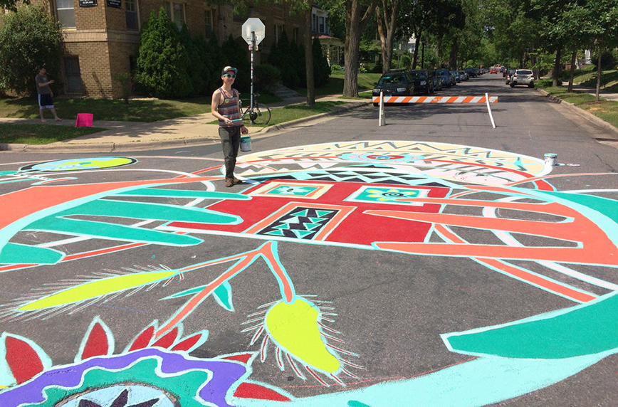 Brightly colored mural on a street intersection and man holding a paint can.