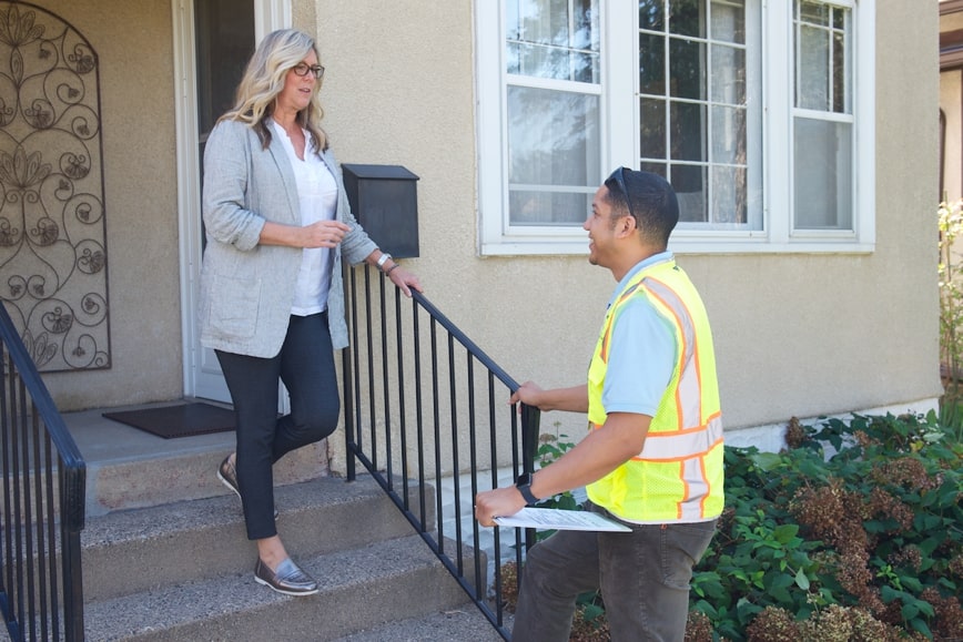 Person in yellow vest talking to person standing on steps in front of house