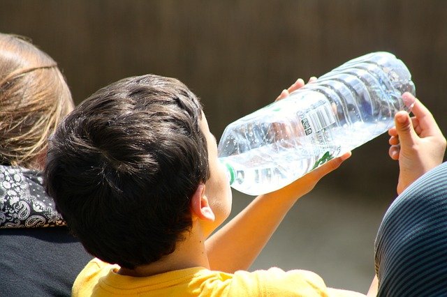 Young child drinking water from large plastic bottle