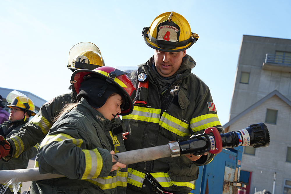 A community member participates in a hose demonstration with a Minneapolis firefighter A community member participates in a hose demonstration with a Minneapolis firefighter