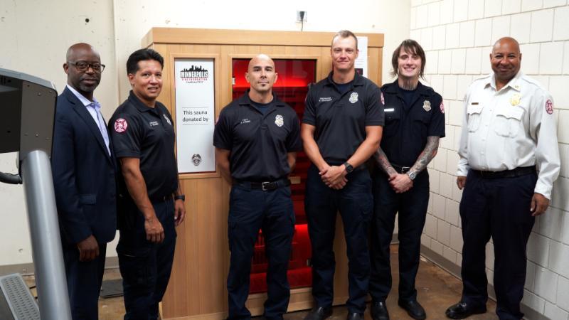 A group of firefighters and city leadership pose in front of a donated sauna. A group of firefighters and city leadership pose in front of a donated sauna.