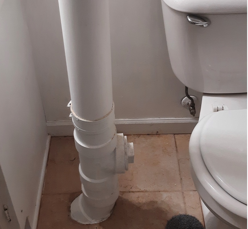 White vertical pipe between toilet and wall