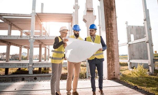 Three workers in yellow vests looking at plan set in front of construction site