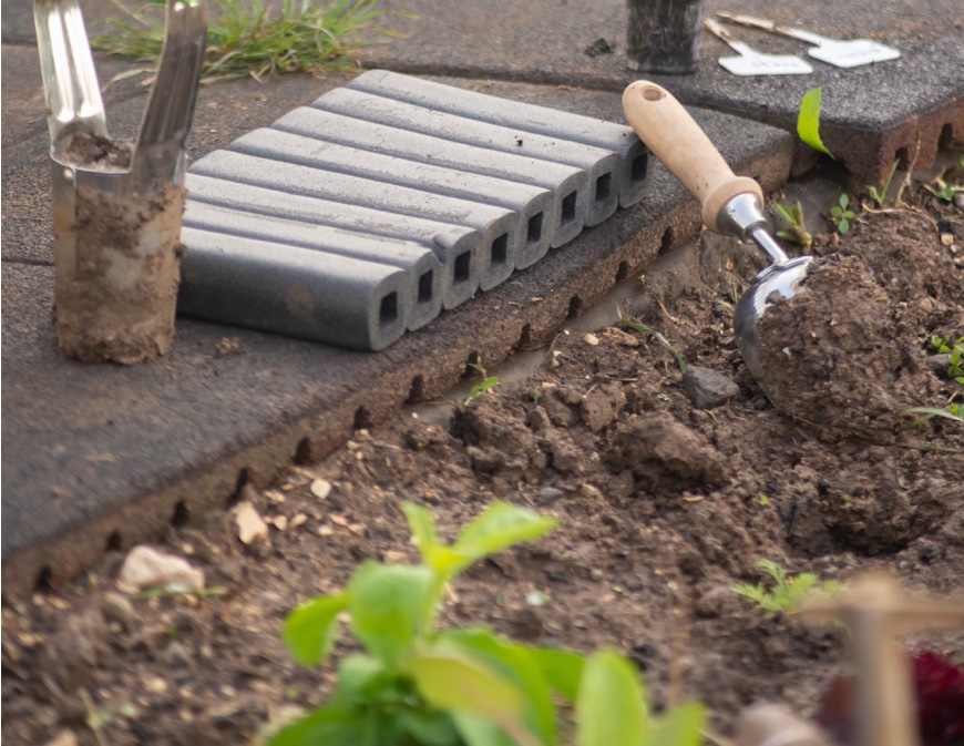 soil abutting sidewalk with trowel and other garden tools nearby