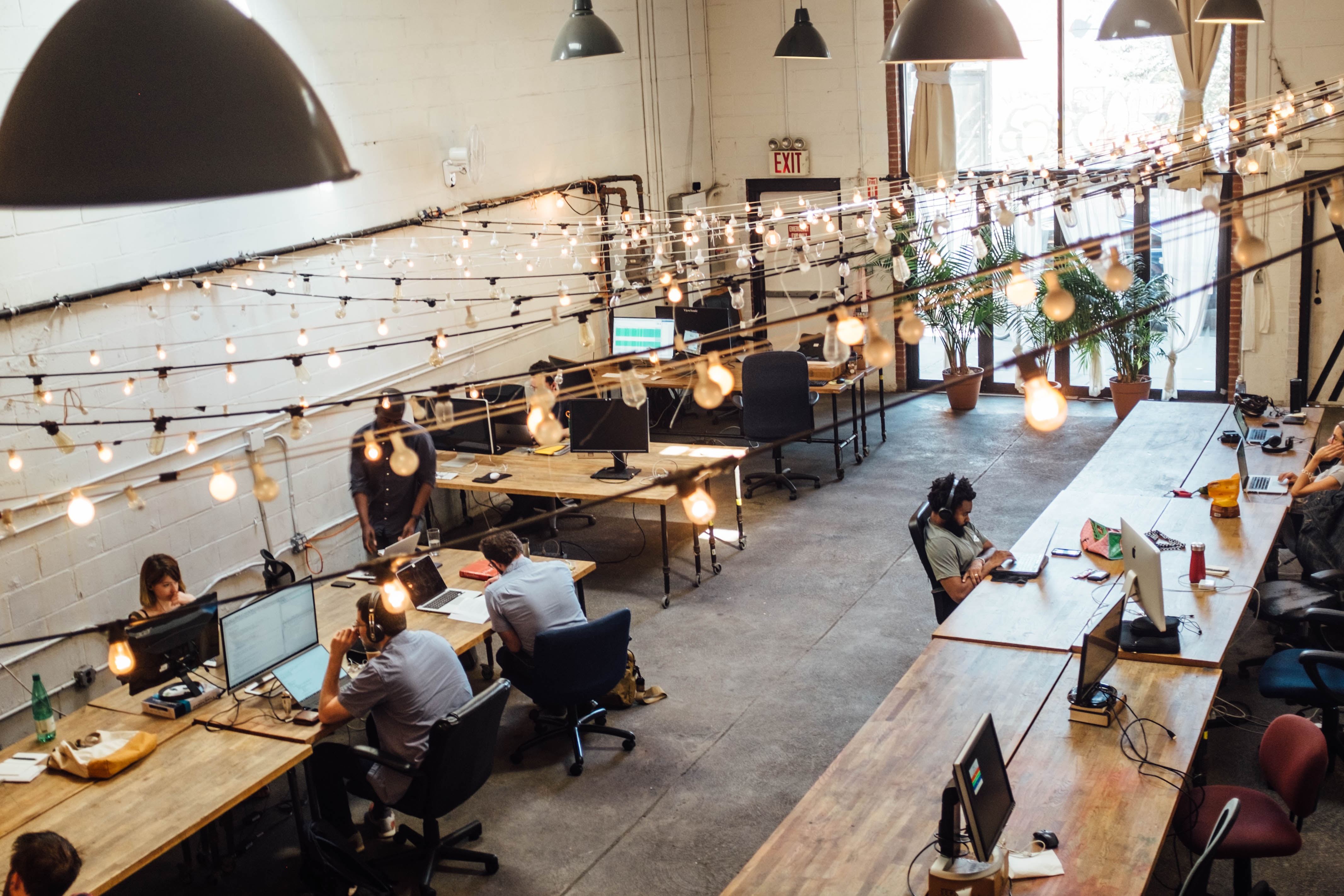 View of open indoor workspace with many workstations and workers.