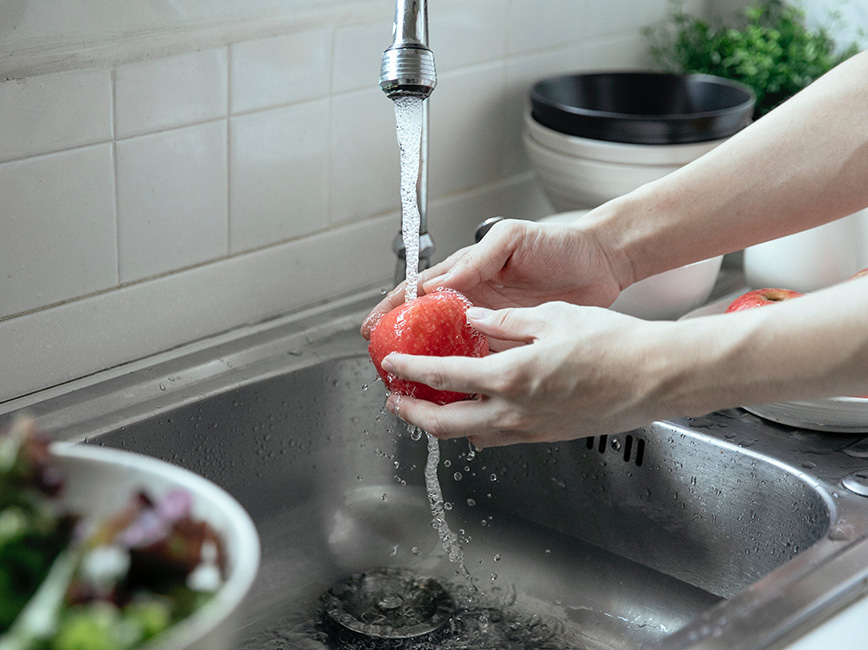 A person washing food in a sink under running water.