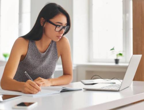 Woman with glasses looking at her laptop taking notes Woman with glasses looking at her laptop taking notes