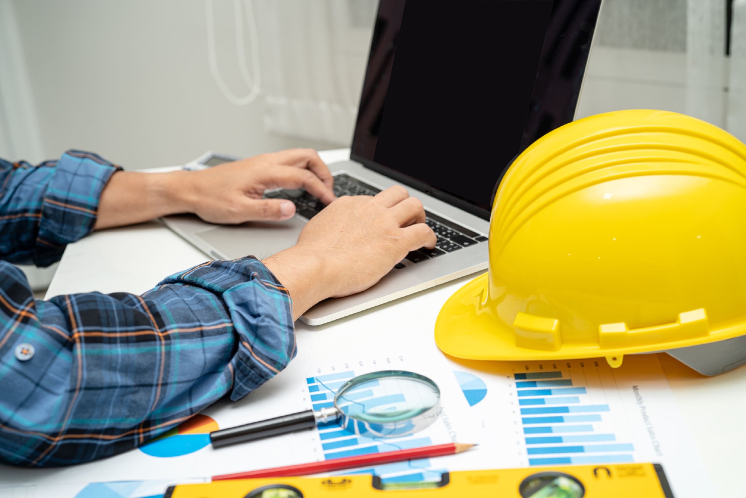 Hands on laptop near yellow construction hat Hands on laptop near yellow construction hat