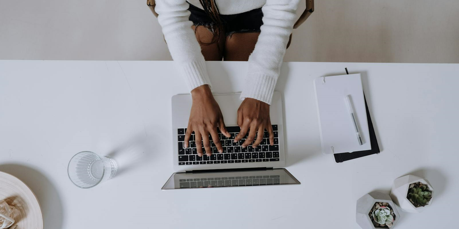 Person typing on laptop with notepad on desk Person typing on laptop with notepad on desk