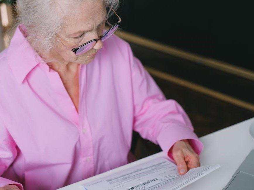 Elderly person reading paper in front of laptop
